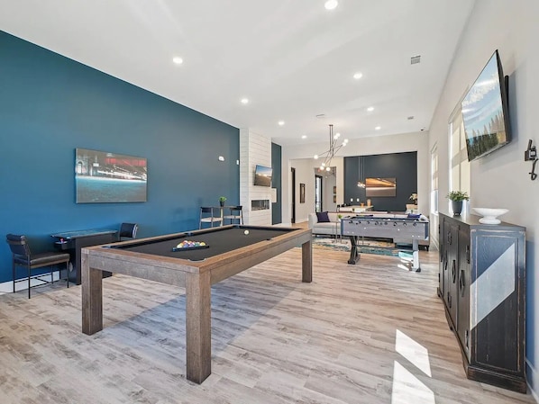 A modern living room with a pool table, a sofa, and a foosball table.