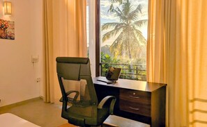 A room with a desk, chair, and a window with a view of palm trees.