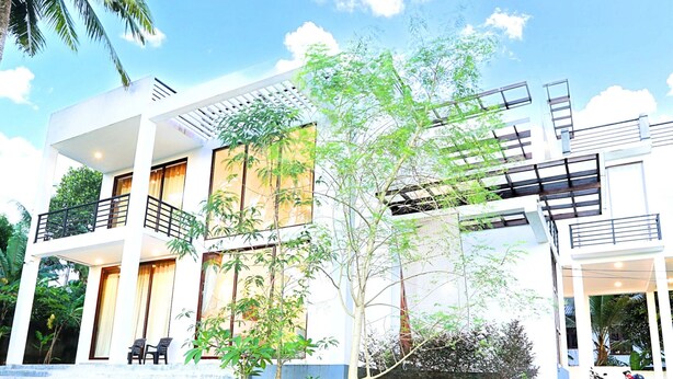 A modern two-story building with balconies, a garden area with small trees, and a clear sky. - Tranquil Heaven (Galle)