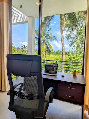 A room with a desk, a laptop, and a view of a tropical landscape.