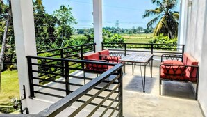 A covered outdoor seating area with a table and chairs, a railing, and a view of greenery and palm trees. - Tranquil Heaven (Galle)