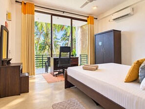 Habitación de hotel con cama, escritorio, armario y vista a palmeras a través de la ventana.