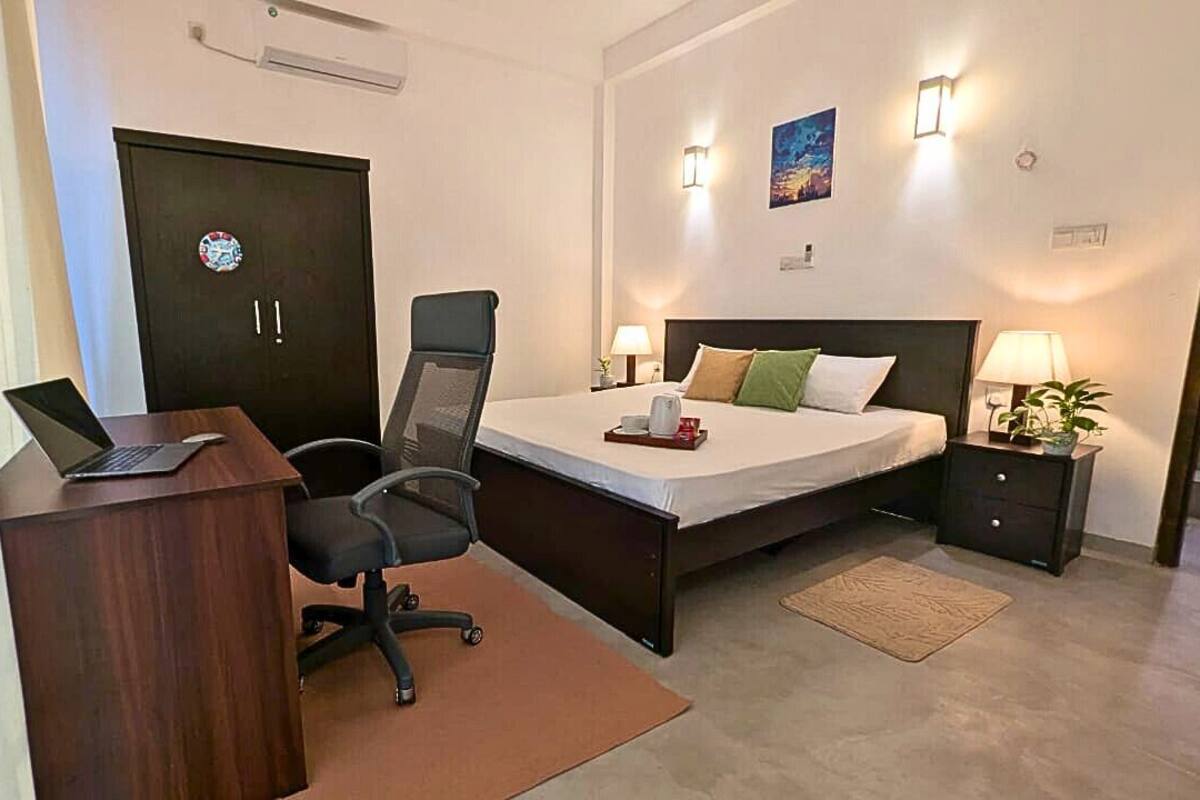 A hotel room with a desk, chair, bed, bedside tables, and a door.