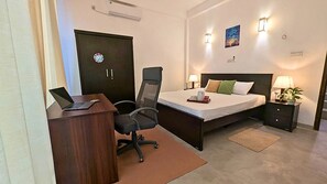 A hotel room with a desk, chair, bed, bedside tables, and a door.
