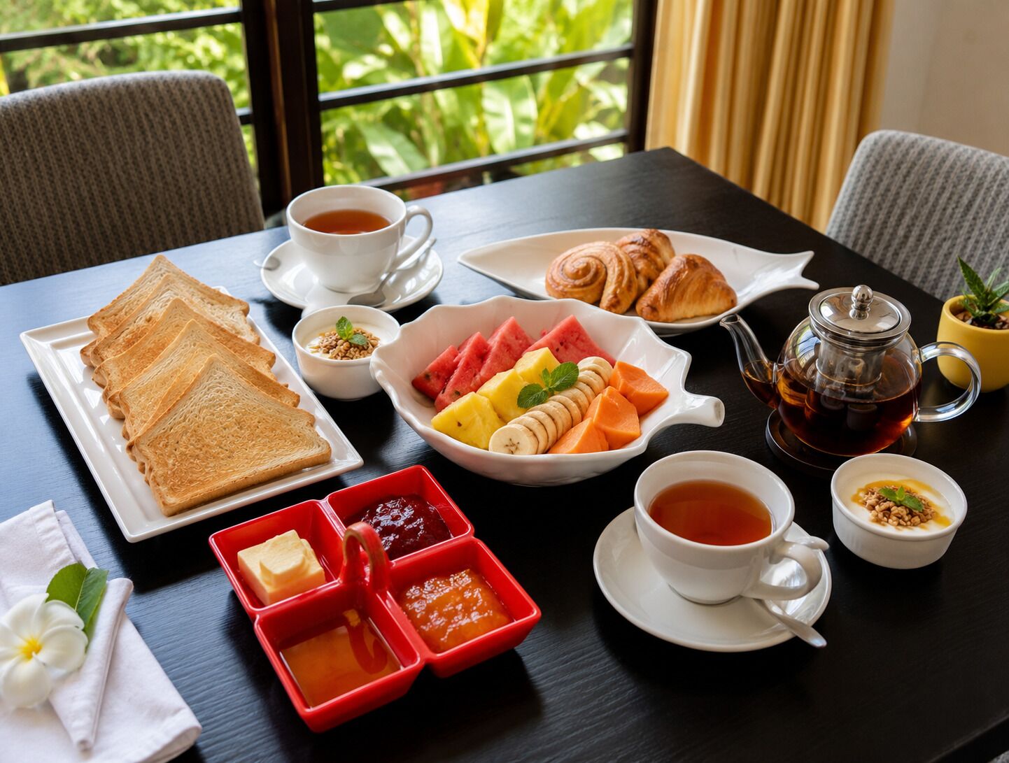 A breakfast setting with toast, croissants, fruit, jam, tea, and a teapot on a table.