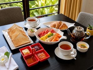 A breakfast setting with toast, croissants, fruit, jam, tea, and a teapot on a table.