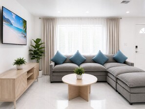 A modern living room with a sectional sofa, a coffee table, a TV, and a potted plant.