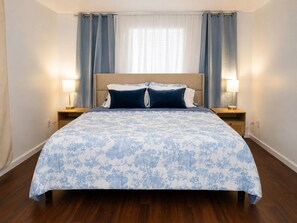 Une chambre Ă coucher avec un lit, deux tables de chevet et une fenĂȘtre avec des rideaux.