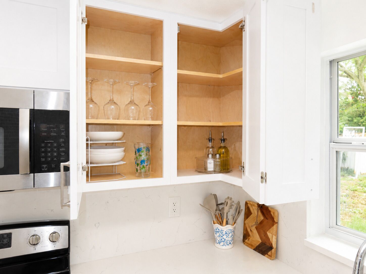 A kitchen with a microwave, stove, and open cabinets containing wine glasses, plates, and kitchen utensils.