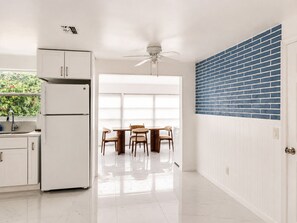 Une cuisine avec des meubles blancs, un rĂ©frigĂ©rateur, un coin repas avec une table et des chaises, et un mur dâaccent en briques bleues.