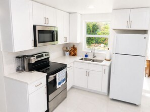 Una cocina moderna con armarios blancos, horno de acero inoxidable, microondas, pileta y refrigerador.