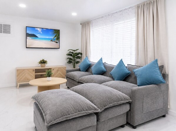 Un salon moderne avec un canapé gris, une table basse ronde et un téléviseur fixé au mur.
