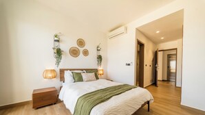 A bedroom with a wooden floor, a bed with a green throw, bedside lamps, and wall-mounted decor. - Modern Studio Downtown Pool & Lake View + Gym Central Park (Punta Cana)