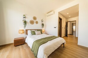 A bedroom with a wooden floor, a bed with a green throw, bedside lamps, and wall-mounted decor. - Modern Studio Downtown Pool & Lake View + Gym Central Park (Punta Cana)
