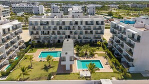 A modern hotel with multiple floors, a central swimming pool, and surrounding greenery. - Modern Studio Downtown Pool & Lake View + Gym Central Park (Punta Cana)