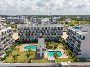 A modern hotel with multiple floors, a central swimming pool, and surrounding greenery. - Modern Studio Downtown Pool & Lake View + Gym Central Park (Punta Cana)