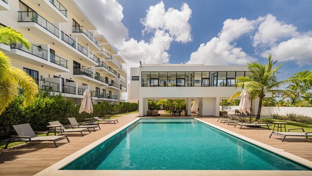 A modern hotel with a swimming pool, multiple balconies, and outdoor seating areas. - Modern Studio Downtown Pool & Lake View + Gym Central Park (Punta Cana)