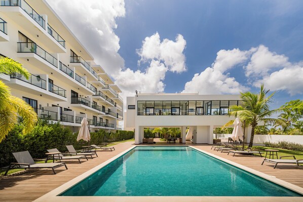 A modern hotel with a swimming pool, multiple balconies, and outdoor seating areas. - Modern Studio Downtown Pool & Lake View + Gym Central Park (Punta Cana)