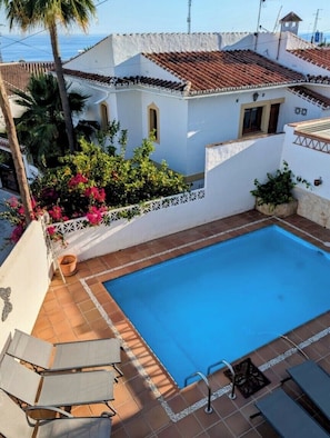 A swimming pool with a tiled deck, lounge chairs, and a white building with a red-tiled roof. - Spacious 3-bedroom house in charming Nerja with pool and walled gardens. (Nerja)