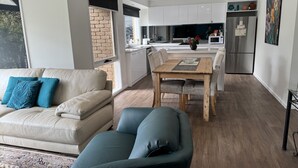 A modern living room with a sofa, a dining table, and a kitchen in the background. - CountrysideRetreat Romance Luxury Cottage NativeWildlife Daylesford – Hepburn (Hepburn)
