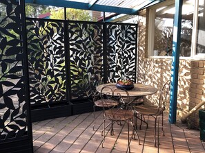 En terrasse med et metalbord og stole, et dekorativt sort hegn og en murstensvæg.
