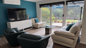 A living room with a TV, sofa, chairs, and a view through large glass doors. - CountrysideRetreat Romance Luxury Cottage NativeWildlife Daylesford – Hepburn (Hepburn)