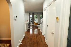 A hallway with wooden flooring, white walls, and a door on the right. - Spacious 3 Bedroom Home in McKenzie Towne (Calgary)