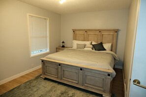 A bedroom with a large bed, a nightstand, a lamp, and a window with blinds. - Spacious 3 Bedroom Home in McKenzie Towne (Calgary)