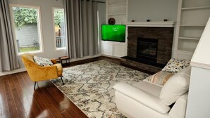 Ein Wohnzimmer mit Kamin, Fernseher, einem gelben Sessel und einem Teppich mit Muster.