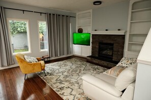 A living room with a fireplace, a television, a yellow armchair, and a patterned rug. - Spacious 3 Bedroom Home in McKenzie Towne (Calgary)