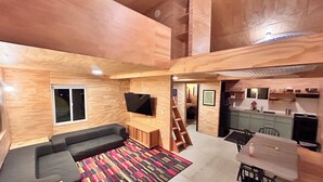 Un espacio habitable en varios niveles con sofá, televisión, zona de cocina y una escalera.