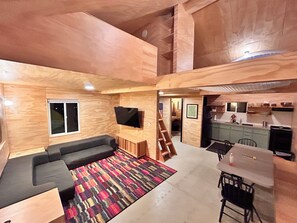 Et flerniveaumiljø med sofa, TV, et køkkenområde og en trappe.