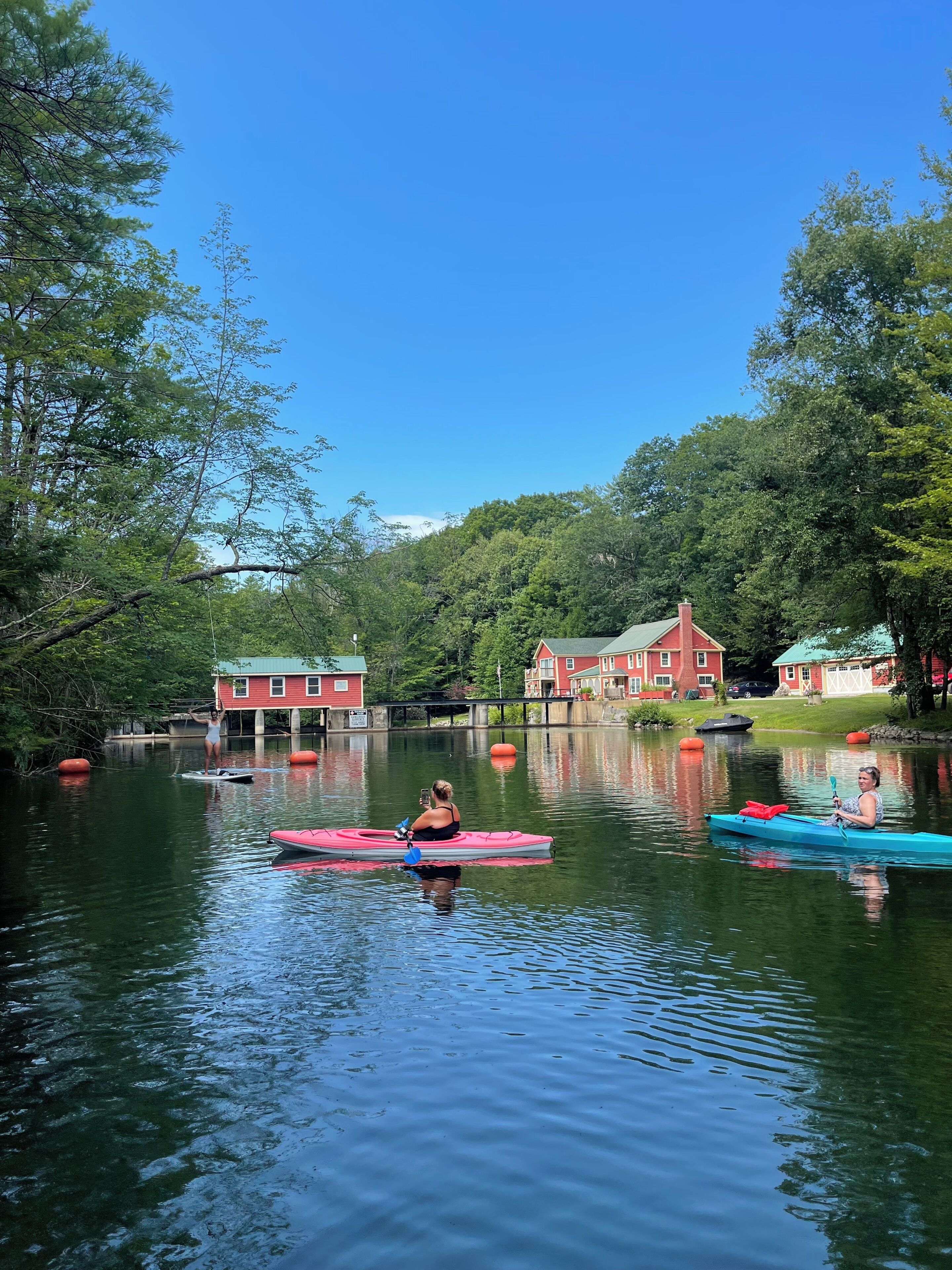 A calm lake with paddle boats, surrounded by trees and houses with red roofs.