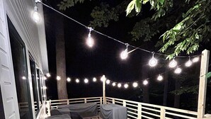 Una terraza de madera con luces colgantes, asientos exteriores y barandilla.