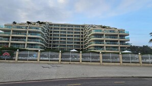 A multi-story building with balconies, a gated entrance, and a clear sky. - Beachfront apartment with ocean view in Recreio. (Rio de Janeiro)