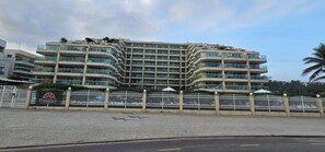A multi-story building with balconies, a gated entrance, and a clear sky. - Beachfront apartment with ocean view in Recreio. (Rio de Janeiro)