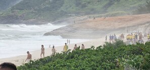 A beach with rocky terrain and vegetation in the foreground. - Beachfront apartment with ocean view in Recreio. (Rio de Janeiro)