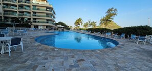 Une piscine avec des chaises longues et, en arrière-plan, un immeuble à plusieurs étages.