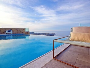 Ein Pool mit Meerblick, ein weißer Stuhl und eine gepolsterte Liegefläche.