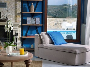 Ein gemütliches Zimmer mit einer Couch, einem Bücherregal, einem Tisch mit Tablett und Blick auf einen Pool und die Landschaft.