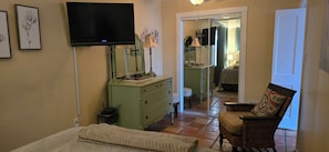 Ein Zimmer mit Fernseher, Kommode, Stuhl und Spiegel.