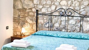 Un llit amb un estovat estampat, dues làmpades de nit i un mur de pedra al fons.