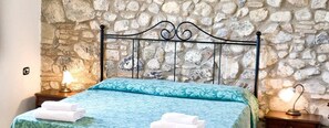 A bed with a patterned bedspread, two bedside lamps, and a stone wall background. - Pomaia - Two Bedroom (Santa Luce)