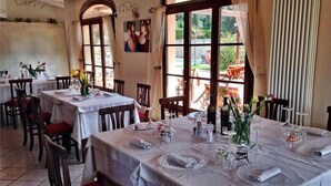 Un restaurant amb diverses taules, caires i grans finestres amb cortines.