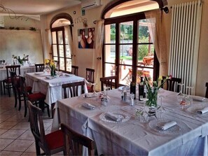 A restaurant with multiple tables, chairs, and large windows with curtains. - Pomaia - Two Bedroom (Santa Luce)
