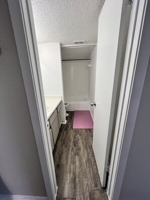 Un corridoio stretto che porta a un bagno con doccia, WC e lavandino.