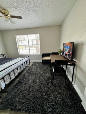 Ein Schlafzimmer mit Bett, Schreibtisch, Stuhl, Deckenventilator, Fenster und einem Bild an der Wand.