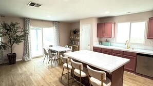 A spacious kitchen with a central island, wooden flooring, and a dining area with chairs.