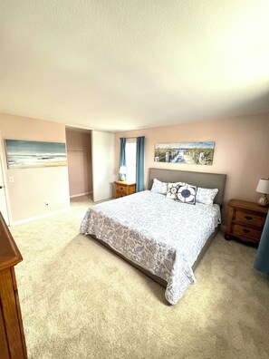 Un dormitorio con una cama grande, una mesita de noche, un aparador, un cuadro y vistas a la playa.