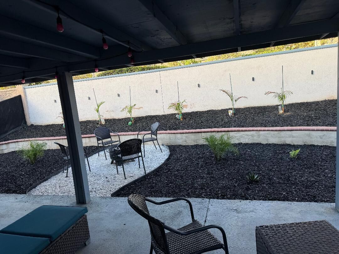 Área de pátio externa com assentos e plantas jovens.